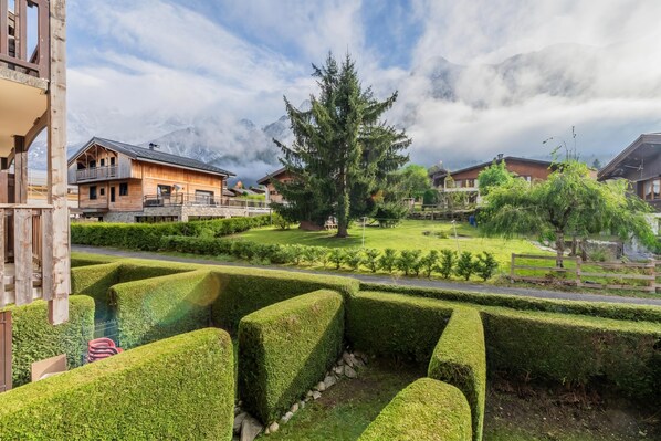 A residential area with wooden houses, a well-maintained hedge, and a large evergreen tree.