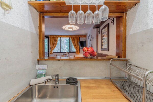 A kitchen with a stainless steel sink, wooden countertop, and a hanging wine glass rack.