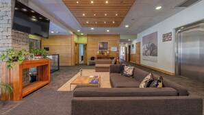 Un vestíbulo moderno con techo de madera, un televisor de pantalla plana montado en una pared de piedra, un sofá, una mesa de centro y un mostrador de recepción.
