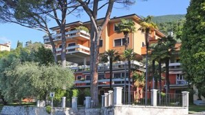 A multi-story residential building with balconies, surrounded by trees and a stone wall. - Roby loft-Direct Lake Access/Beach, Gardone Riviera, Italy (Gardone Riviera)