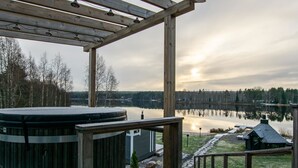 Eine Holzterrasse mit Whirlpool mit Blick auf einen stillen See und einen bewaldeten Uferbereich.