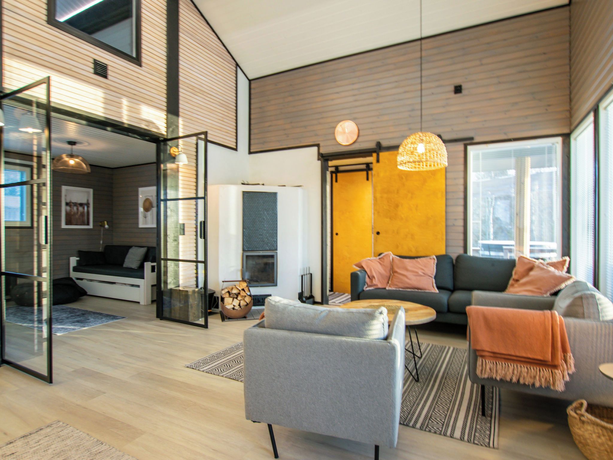 A modern living room with a sofa, armchair, and coffee table. There is a fireplace and a glass door leading to another room.