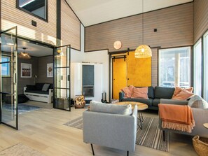 Un salon moderne avec un canapé, un fauteuil et une table basse. On y trouve une cheminée et une porte vitrée qui donne sur une autre pièce.