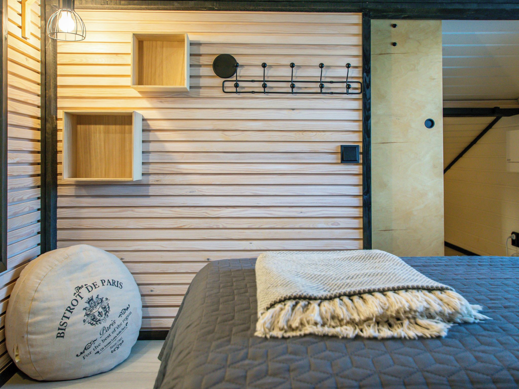Ein Zimmer mit einem Bett, einer Wandregal, einer Hängelampe und einem Kissen mit Aufschrift.