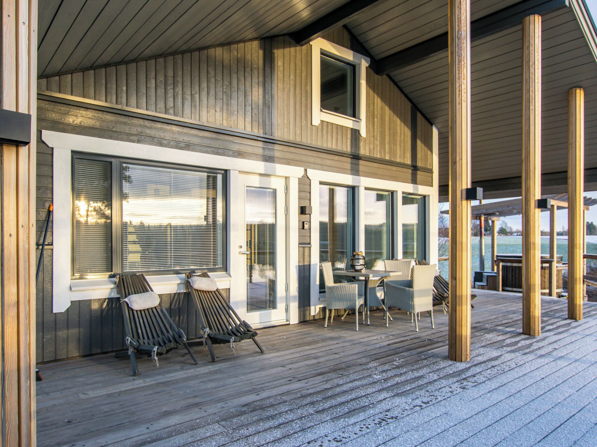 Ein überdachter Außenbereich mit Holzterrasse, einem Tisch mit Stühlen und einer Sitzecke mit Lounge-Möbeln.