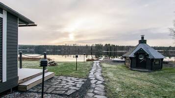 A lakeside property with a stone pathway leading to a small cabin, a wooden deck, and a view of the lake and forest.