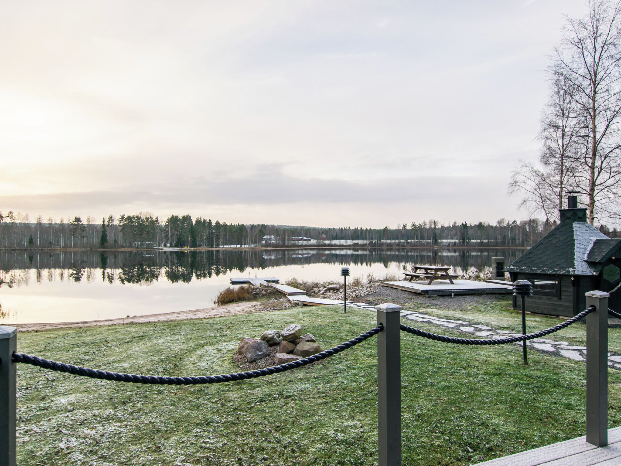 A lakeside view with a wooden dock, picnic area, and a cabin.