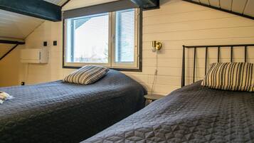 A room with two beds, a window with blinds, a wall-mounted light fixture, and a ceiling with exposed beams.