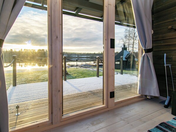 A wooden cabin with a large glass door leading to a deck overlooking a lake.