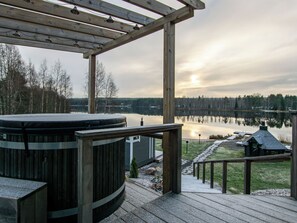 Une terrasse en bois avec un jacuzzi, un chemin de pierre et une vue sur un lac et une forêt.