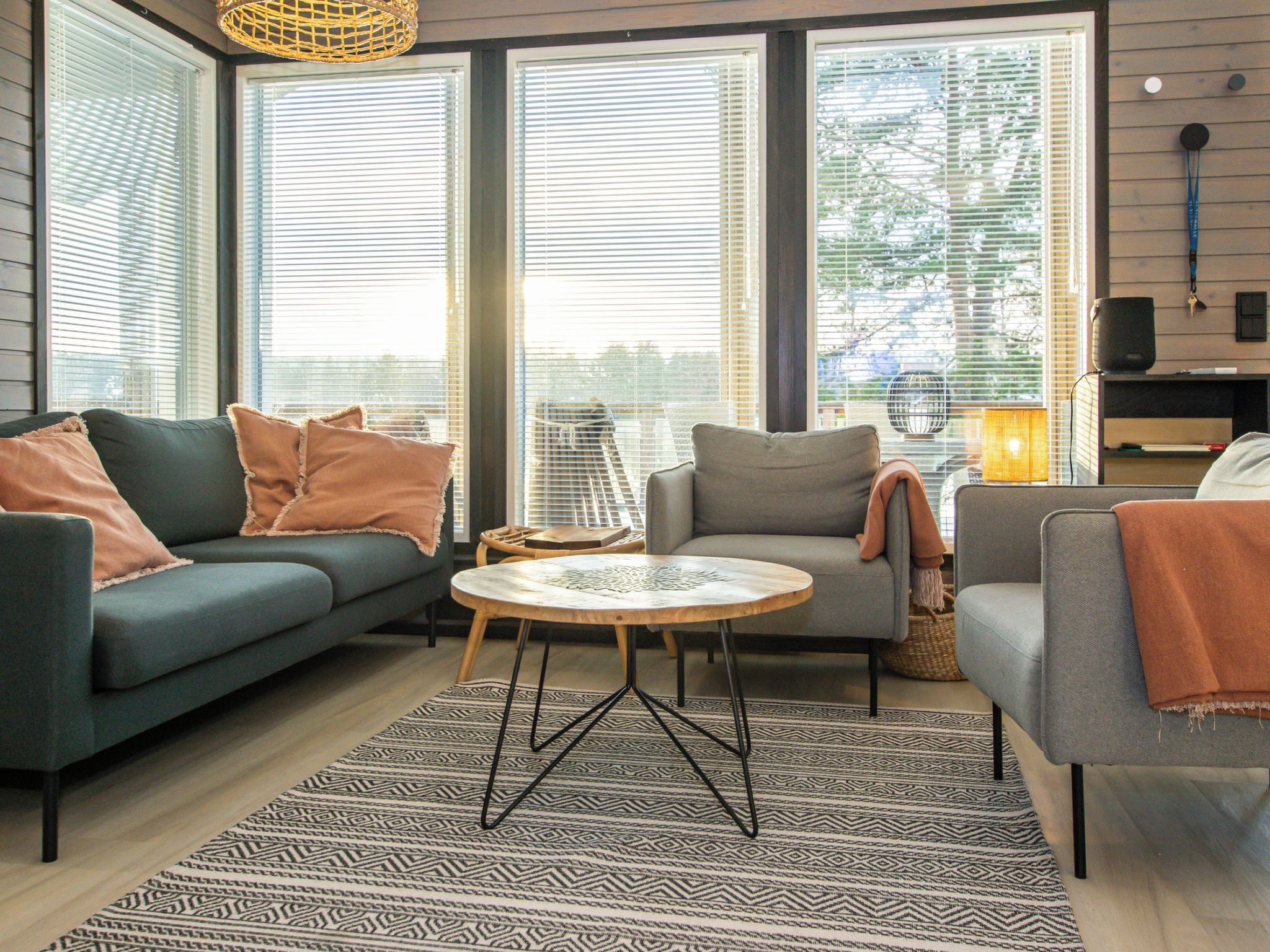A modern living room with a sofa, armchair, and round coffee table, featuring large windows and a patterned rug.