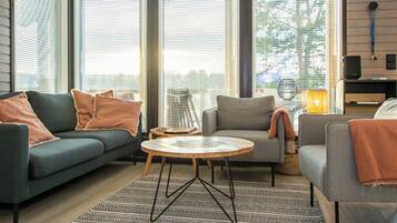 A modern living room with a sofa, armchair, and round coffee table, featuring large windows and a patterned rug.