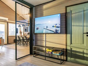 Ein modernes Interieur mit einem an einer Holzwand montierten Fernseher, einem Essbereich mit Stühlen und einem Tisch sowie einer Tür mit Griff.