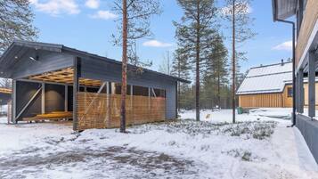 A modern building with an open structure, surrounded by snow-covered ground and tall trees.