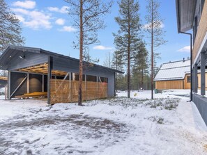 Un edificio moderno con estructura abierta, rodeado de suelo cubierto de nieve y altos árboles.