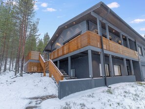 Un bâtiment moderne à plusieurs étages, doté d’un escalier en bois menant à un balcon, entouré de neige et d’arbres.