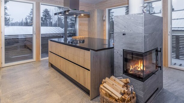 Una cucina moderna con isola centrale, camino a incasso e ampie finestre che si affacciano su un paesaggio innevato.