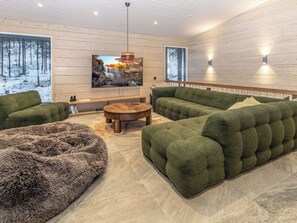 Una sala de estar moderna con un televisor de pantalla plana grande, sofás tapizados en verde, una mesa de centro redonda de madera y una alfombra mullida.