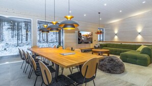 Un'area pranzo moderna con tavolo e sedie in legno, un divano verde e illuminazione a sospensione.