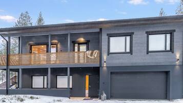 A modern two-story building with a balcony, large windows, and a garage.