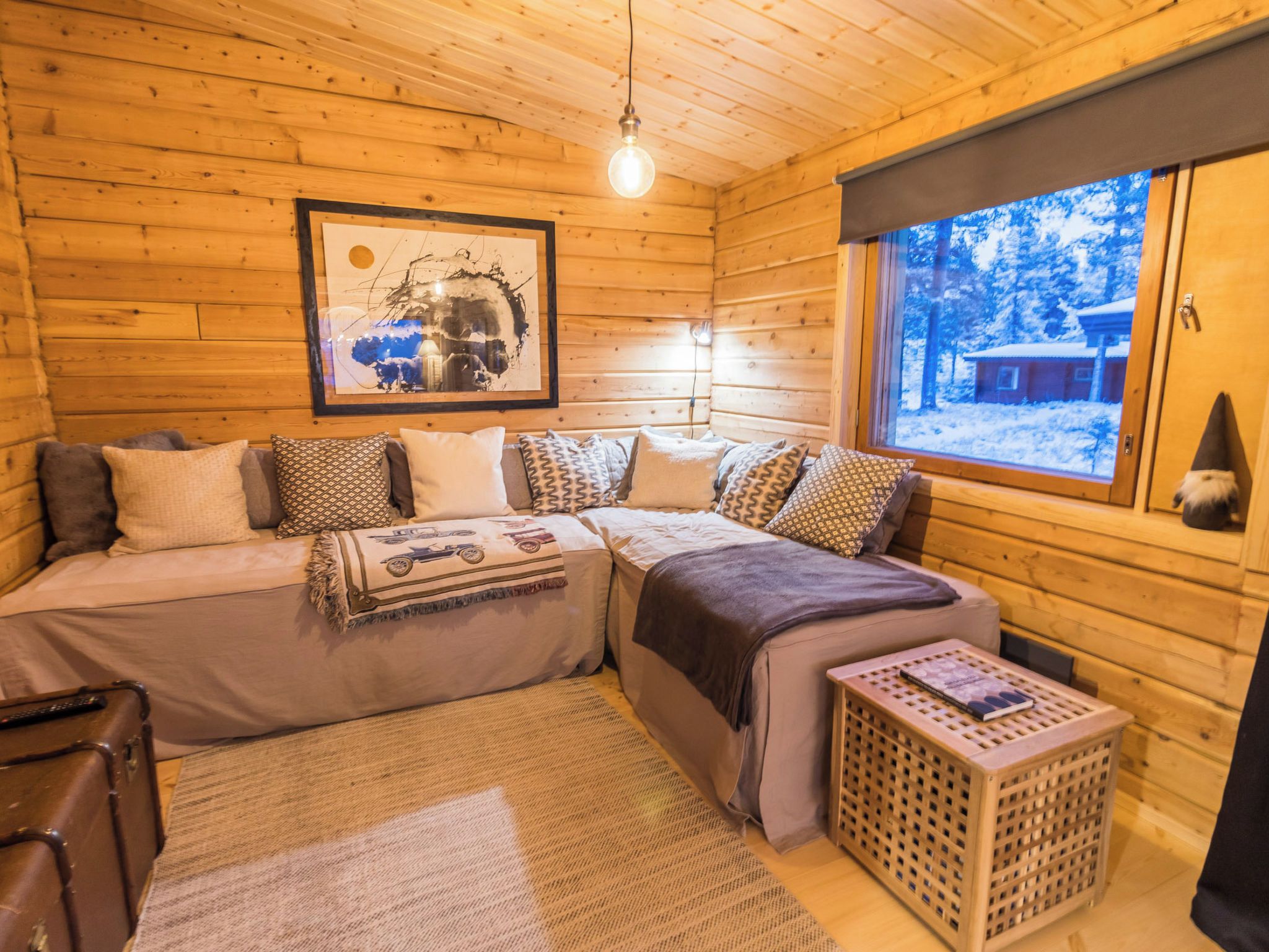 Interior acolhedor de uma cabana, com uma cama, uma obra de arte emoldurada, uma janela com vista para a neve e uma pequena mesa.