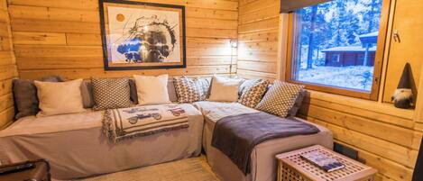 Interior acogedor de una cabaña con una cama, una obra de arte enmarco, una ventana con vistas nevadas y una pequeña mesa.
