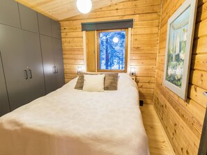A wooden cabin bedroom with a bed, a wardrobe, and a window with a view of trees.