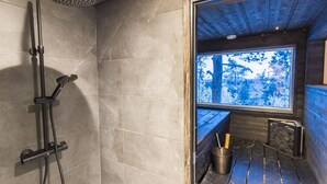 Un baño moderno con ducha, un banco de madera y ventana con vistas a árboles.