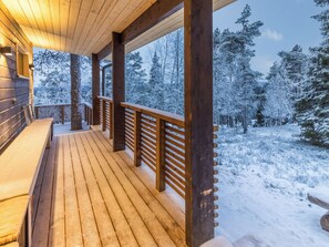 A wooden deck with a railing, benches, and a view of snow-covered trees.