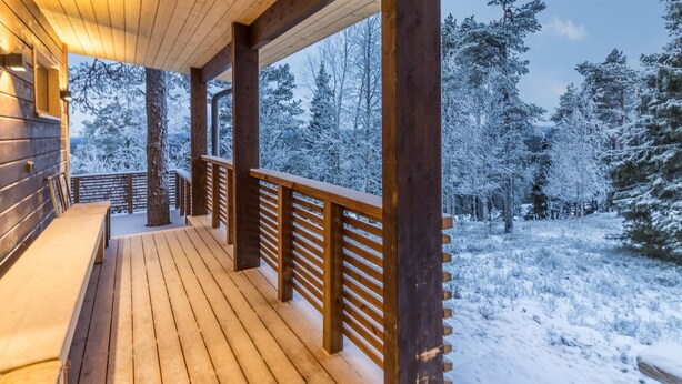 Una terraza de madera con bancos, rodeada de árboles cubiertos de nieve.