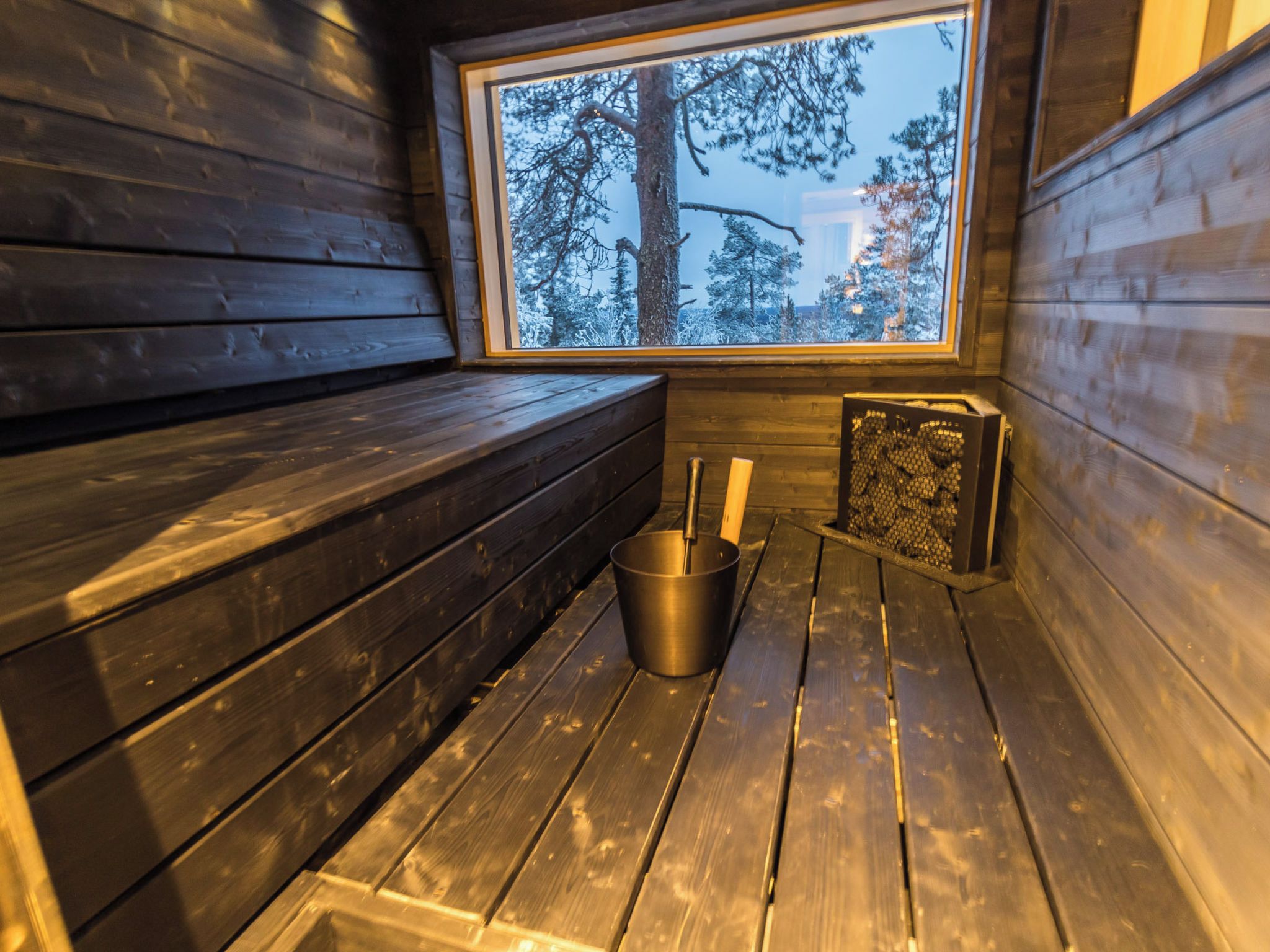 Una sala de sauna con bancos de madera, un cubo de metal y un calentador de sauna.