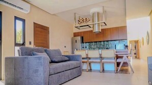 Ein modernes Wohnzimmer mit grauem Sofa, einem Essbereich mit Tisch und Stühlen sowie einer Küche mit Holzschränken.