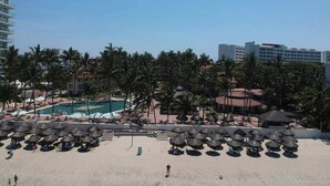 Une plage avec des parasols, une piscine et des palmiers.