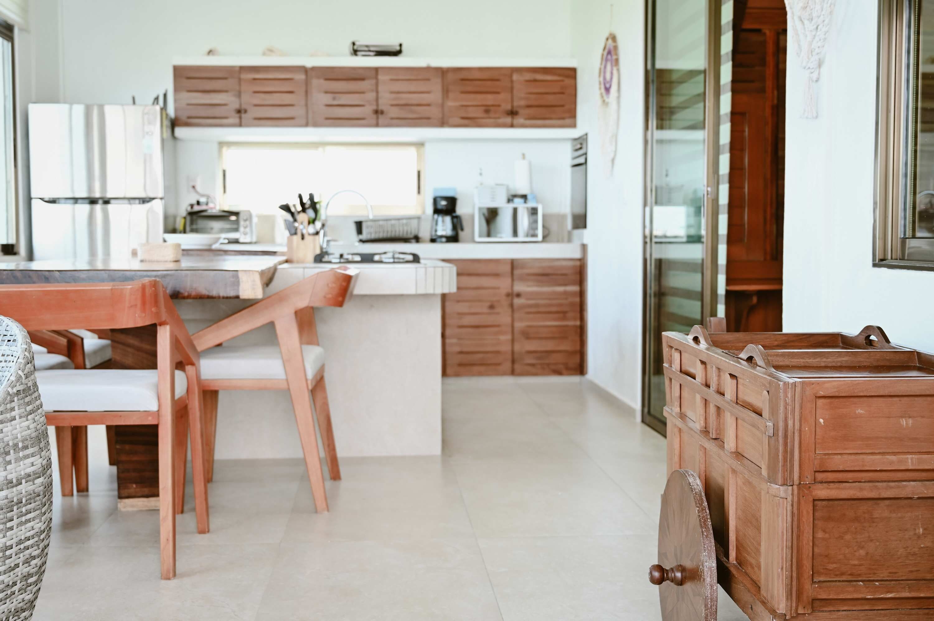 A modern kitchen with wooden cabinets, a central island, and a dining area with chairs.