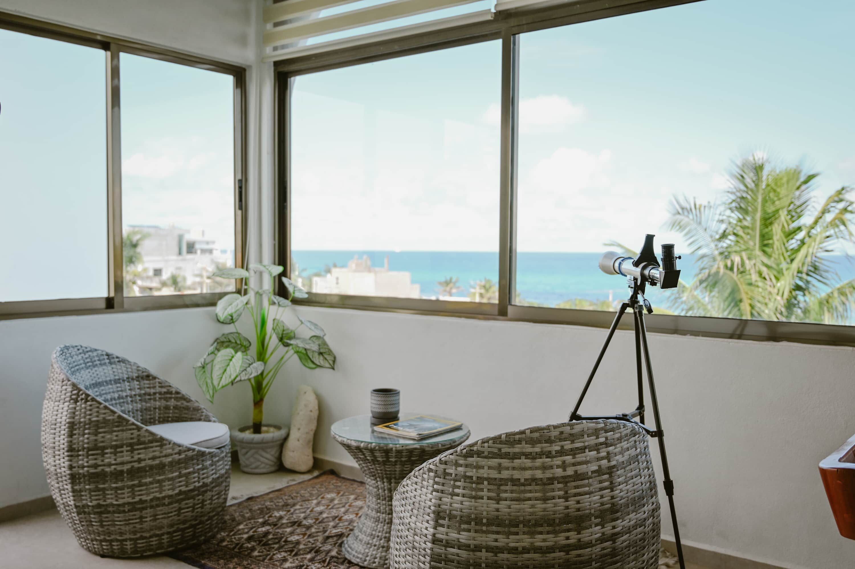 Una habitación con muebles de mimbre, una planta en maceta y un telescopio sobre trípode.