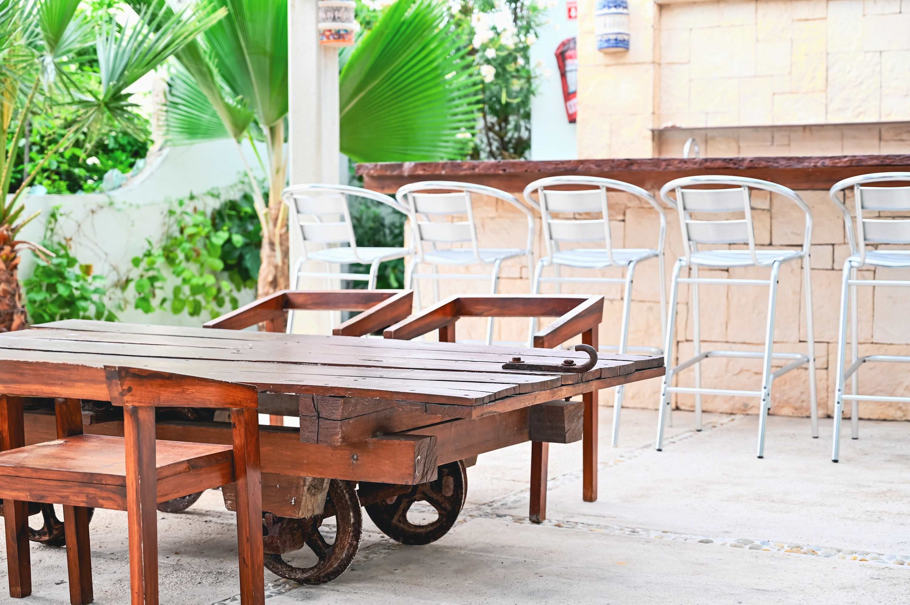 A wooden table with a metal frame, positioned outdoors with chairs and greenery in the background.