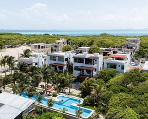 A resort with multiple white buildings, a swimming pool, and a view of the ocean.