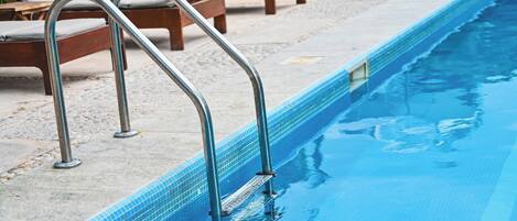 A swimming pool with metal ladders, lounge chairs, and a tiled edge.