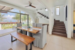 A spacious living area with a dining table, a sofa, a staircase, and a view of the ocean. - Villa · Private Pool · Ocean View · Isla Mujeres (Isla Mujeres)