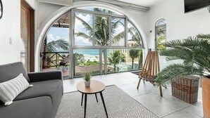 A spacious living area with a large arched window, a sofa, a small table, and a painting easel. - Villa · Private Pool · Ocean View · Isla Mujeres (Isla Mujeres)