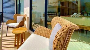 Een balkon met rieten meubilair en een glazen wand die de lucht weerspiegelt.