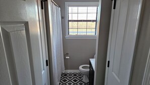 Un baño estrecho con inodoro, una ventana con persianas y baldosas de piso estampadas.