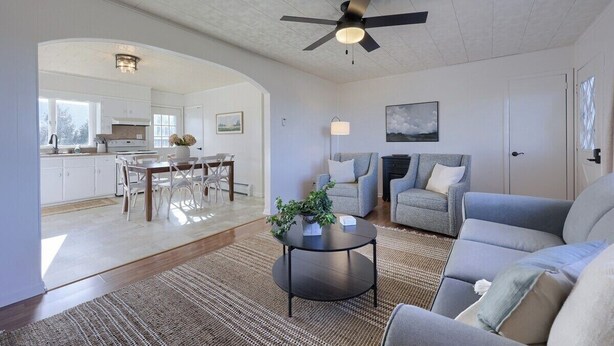 A living room with a sofa, a coffee table, a ceiling fan, and a view into the kitchen.