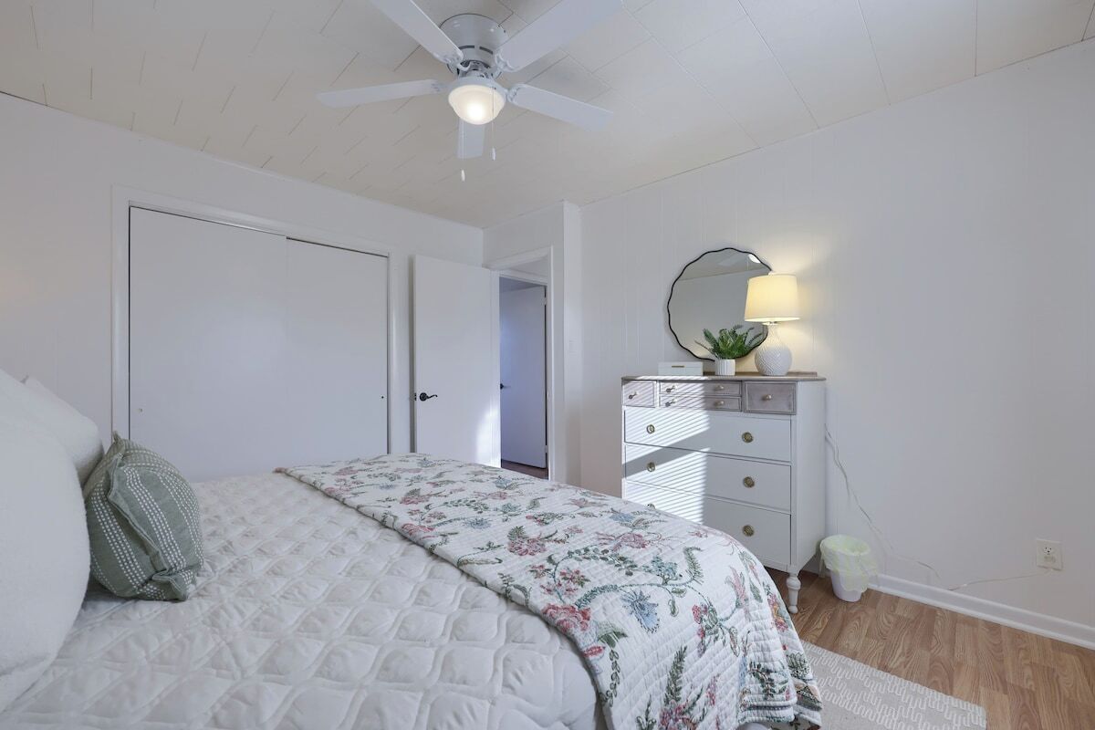 A bedroom with a bed, a dresser, a ceiling fan, and a mirror.