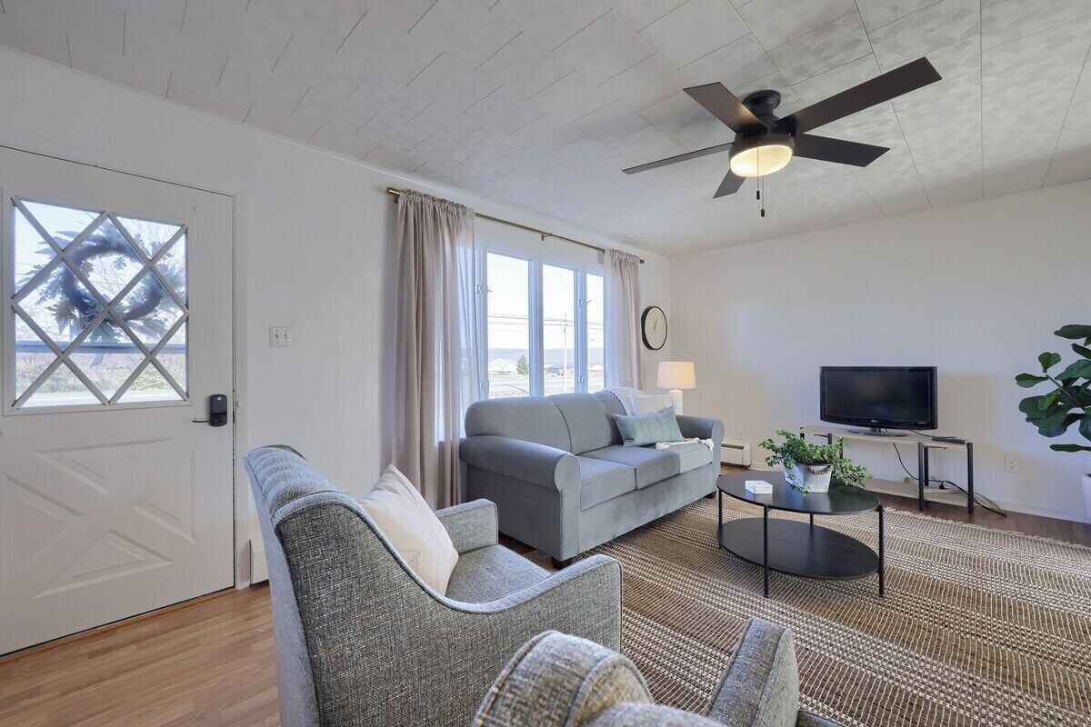 Een woonkamer met een bank, fauteuil, televisie en plafondventilator.