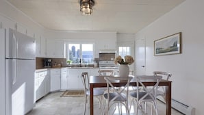 A kitchen with white cabinets, a dining table with chairs, a vase with flowers, and a city view through the window.