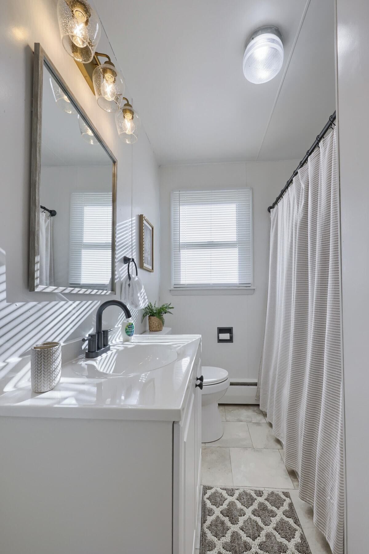 A modern bathroom with a white vanity, a mirror, a sink, a toilet, and a shower curtain.