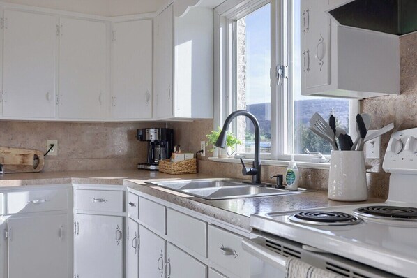 A modern kitchen with white cabinets, a black faucet, a coffee maker, and a window with a view. - Mountain Sunrise Retreat (Spring Glen)