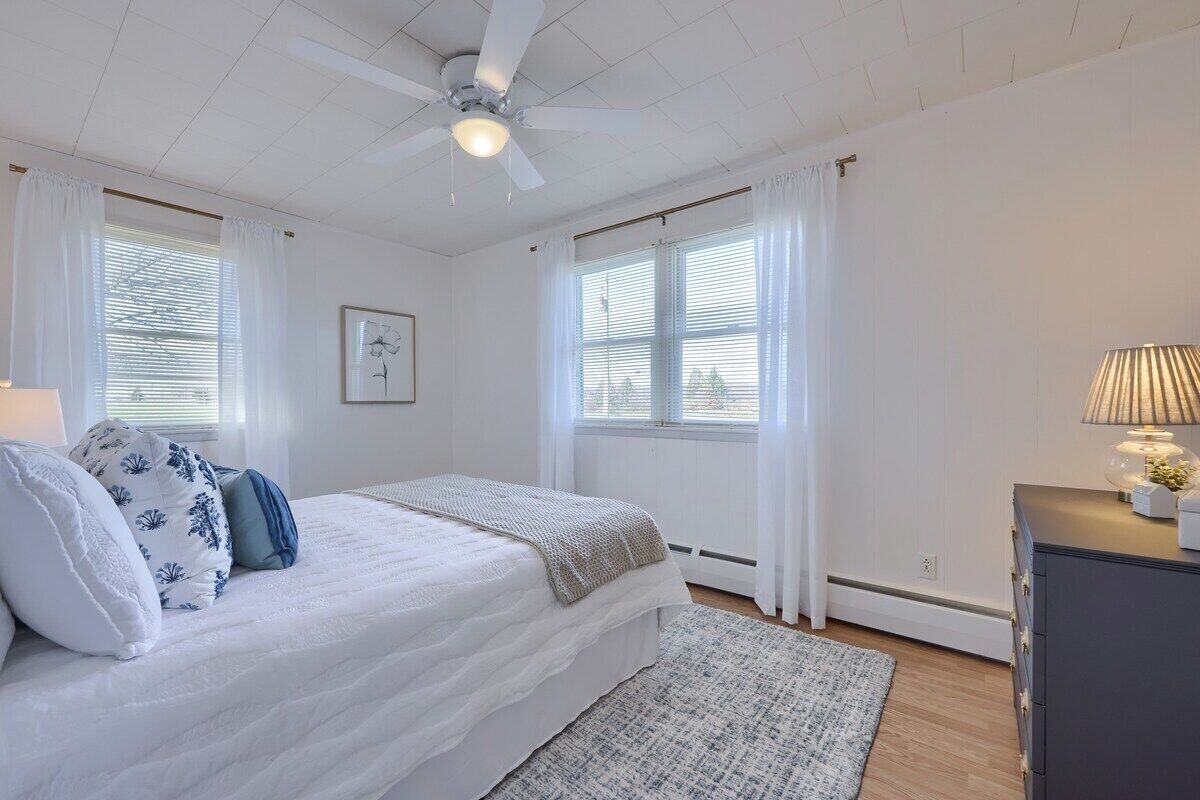 A bedroom with a bed, a ceiling fan, a dresser, and a window with curtains.