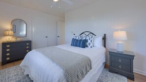 A bedroom with a bed, a dresser, a nightstand, a ceiling fan, and a door.